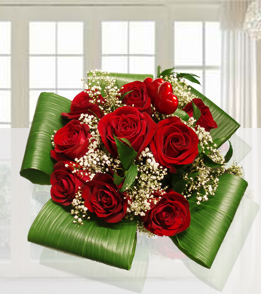 Bouquet di 9 rose rosse fresche con foglie verdi di felce in un vaso di vetro cilindrico su fondo luminoso.